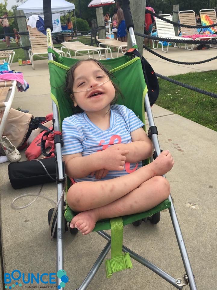 A happy toddler sitting cross-legged in a green stroller outdoors.